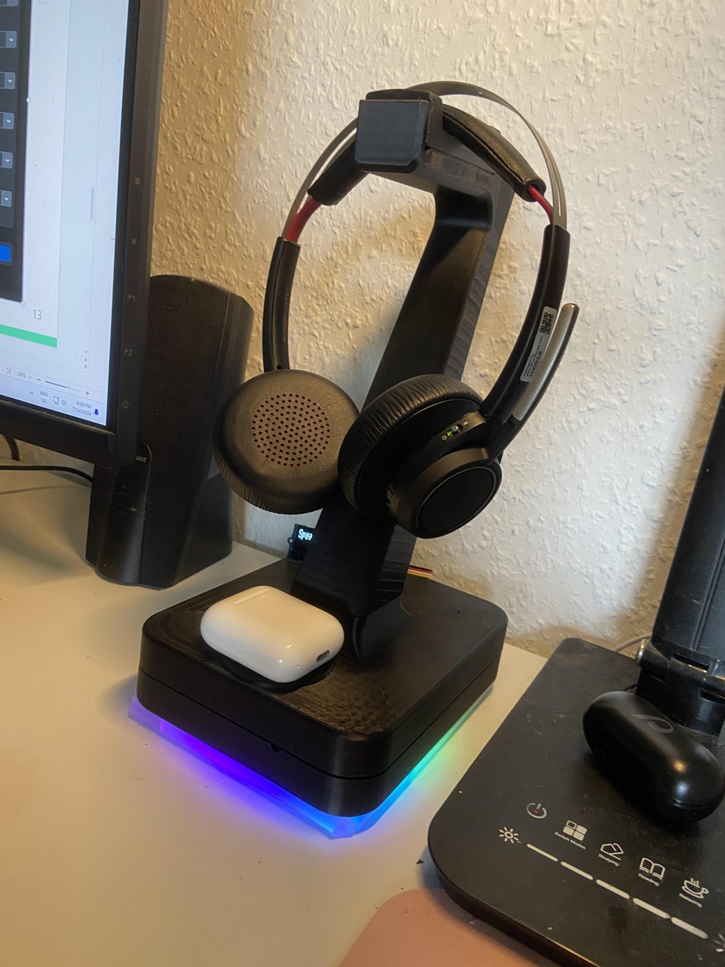 The SmrtStand prototype on a desk: a black 3D-printed stand holding a headset over a base lit in blue